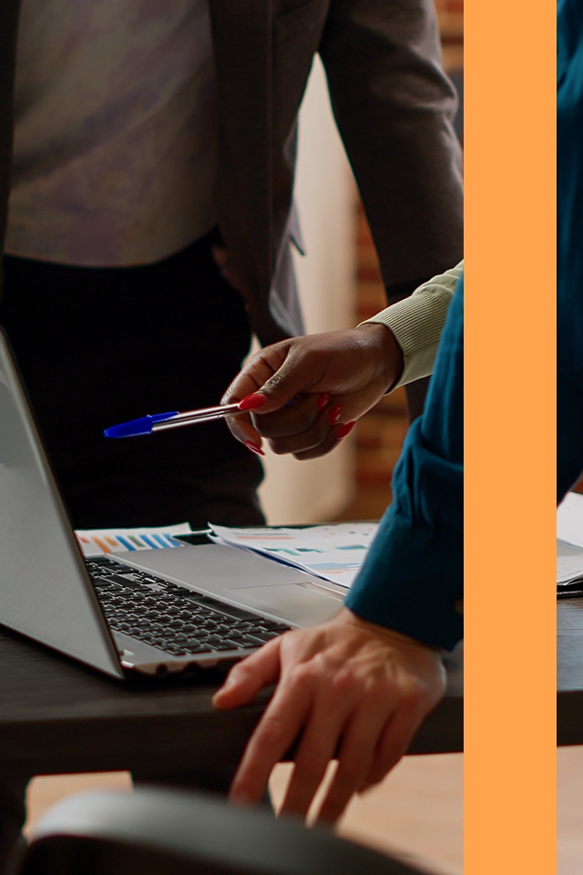 Kvinna som pekar på en bärbar dator med en penna medans hennes kollegor tittar på.