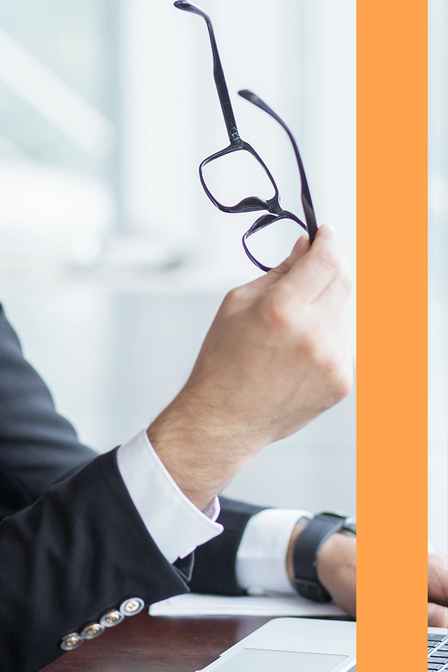 Man som håller i sina glasögon och sitter framför en dator.